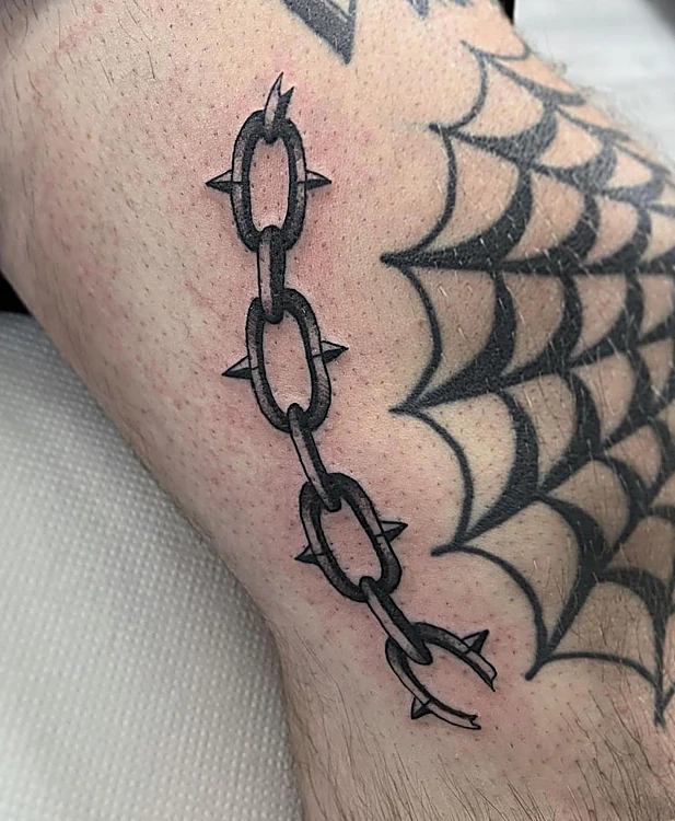 Cadena con púas y telaraña en negro sólido, junto a la rodilla