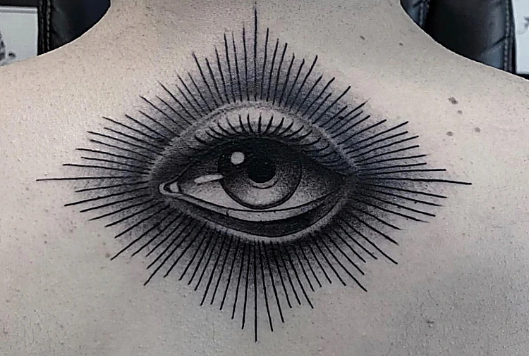 Ojo con rayos finos alrededor, pieza simétrica de blackwork en la espalda alta