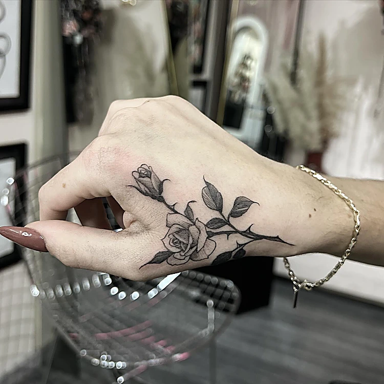 Rosa en línea fina recién tatuada en el dorso de una mano, dentro del estudio, con estantes y espejos al fondo